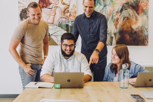 Several smiling people gather around a laptop to build a membership website.