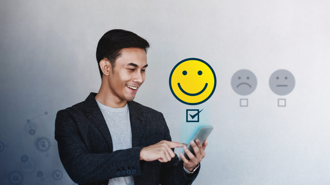 A businessman experiencing a good member experience smiles at the phone he holds while it emits a smiley face icon.